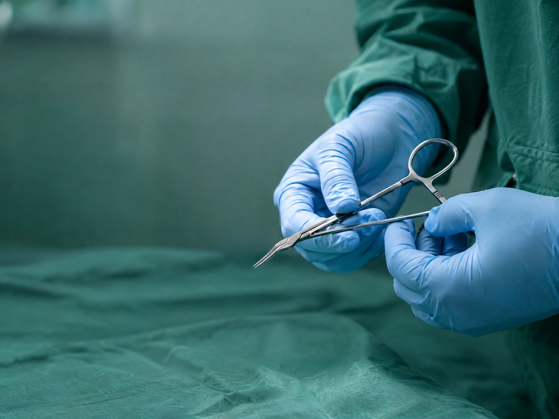 Surgeon's gloved hands holding fine surgical forceps in an operating theatre